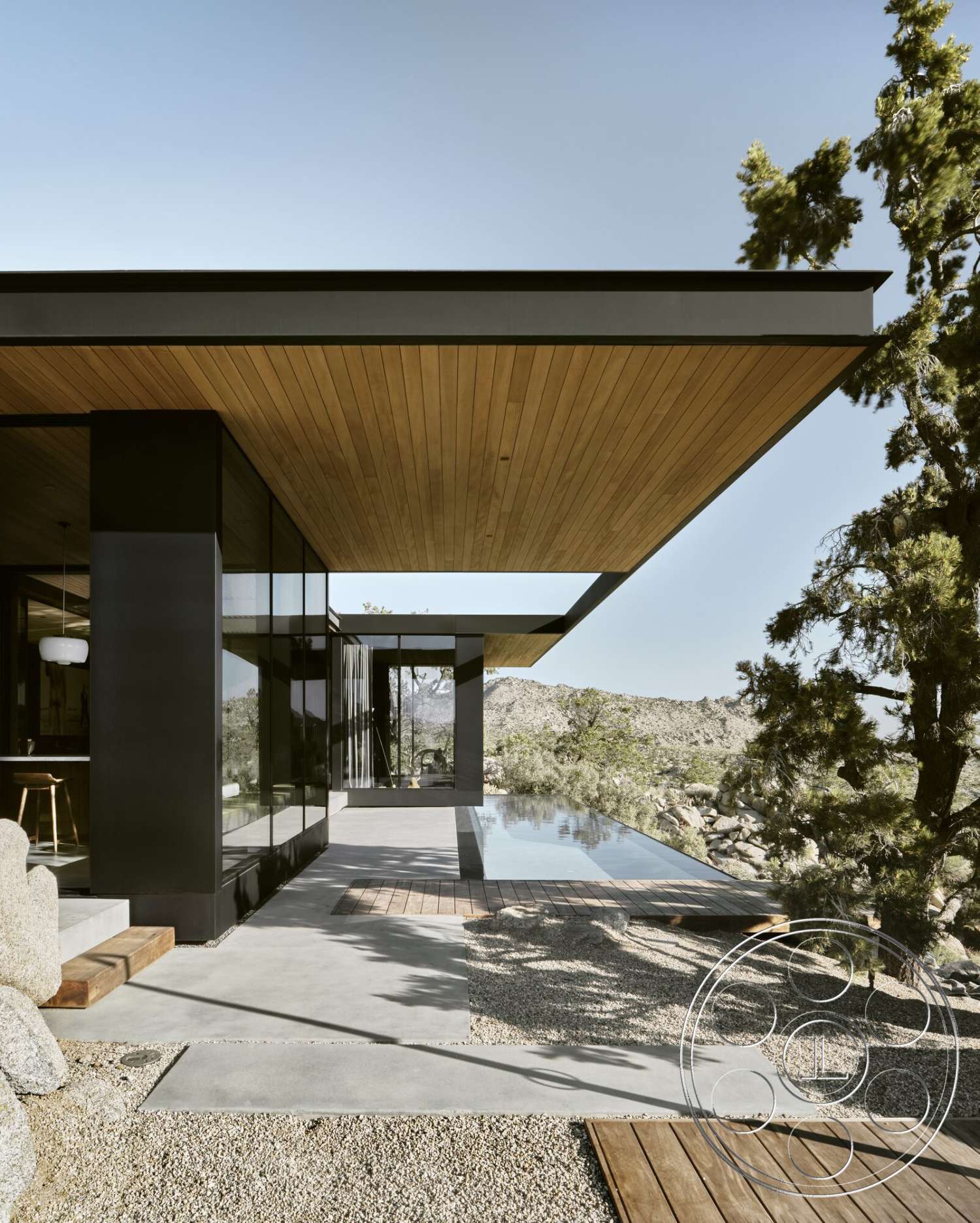 Palm Springs 110 - exterior, large glass windows, gravel landscape, flat roof design, contemporary architectural style, mountain view setting, concrete patio flooring, wood deck area, wood soffit ceiling, black metal wall panels