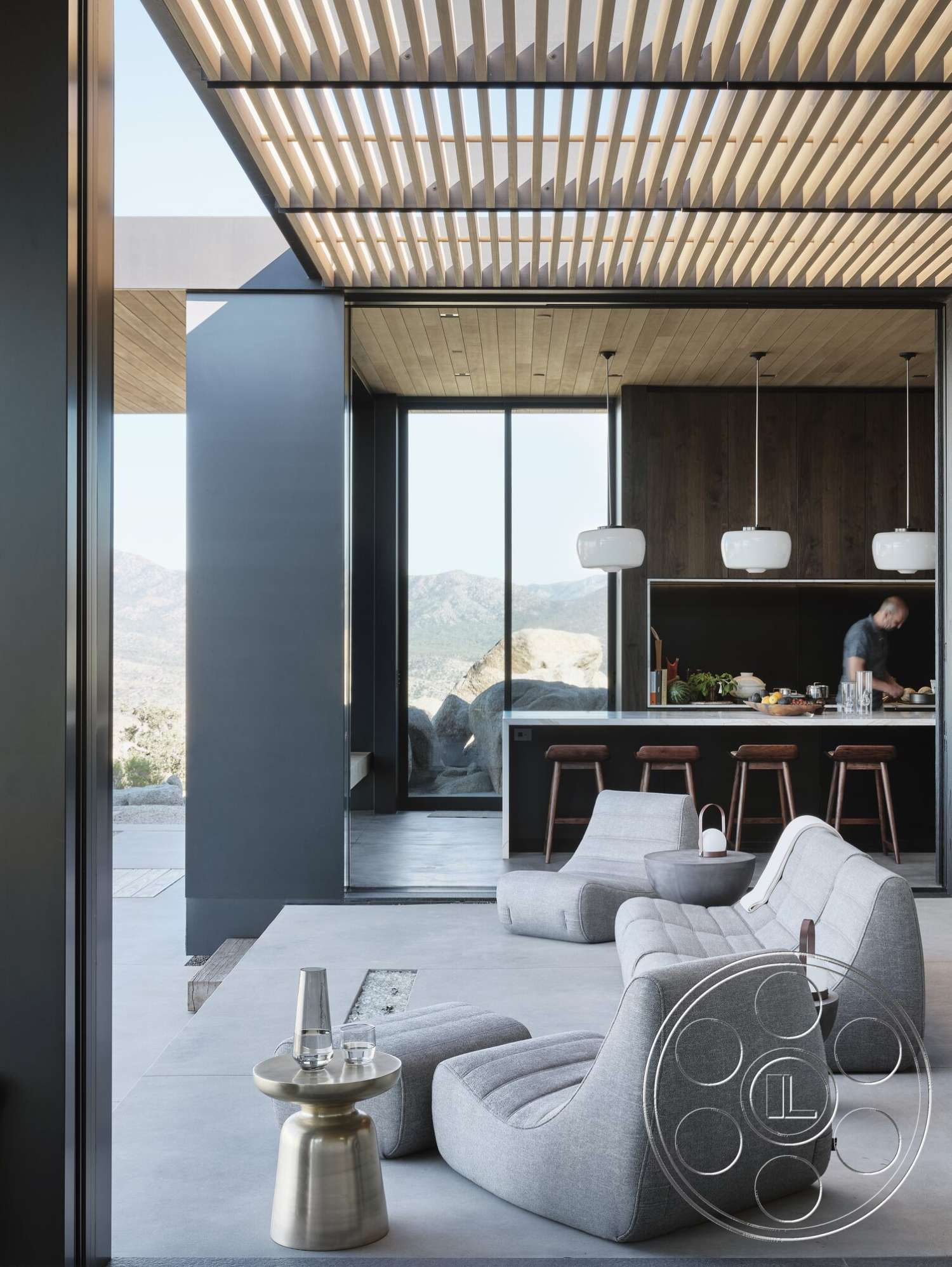 Palm Springs 110 - open floor plan, concrete flooring, minimalist design elements, modern pendant lighting, dark wood accent wall, interior lounge area, exterior mountain view, horizontal wood slat ceiling, modern kitchen with island, curved sofa seating, black glass window walls, brass side table