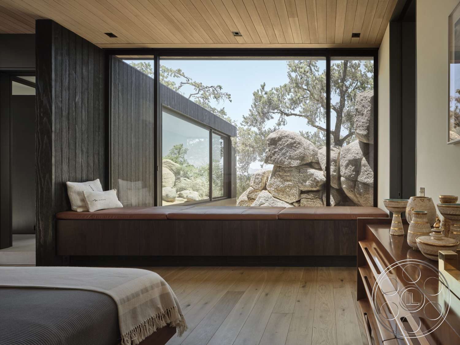 Palm Springs 110 - scenic outdoor view, dark wood paneling walls, minimalist furniture design, floor-to-ceiling glass windows, wood plank ceiling, light hardwood bedroom floors, built-in wooden window seat, natural rock feature wall, mountain retreat setting