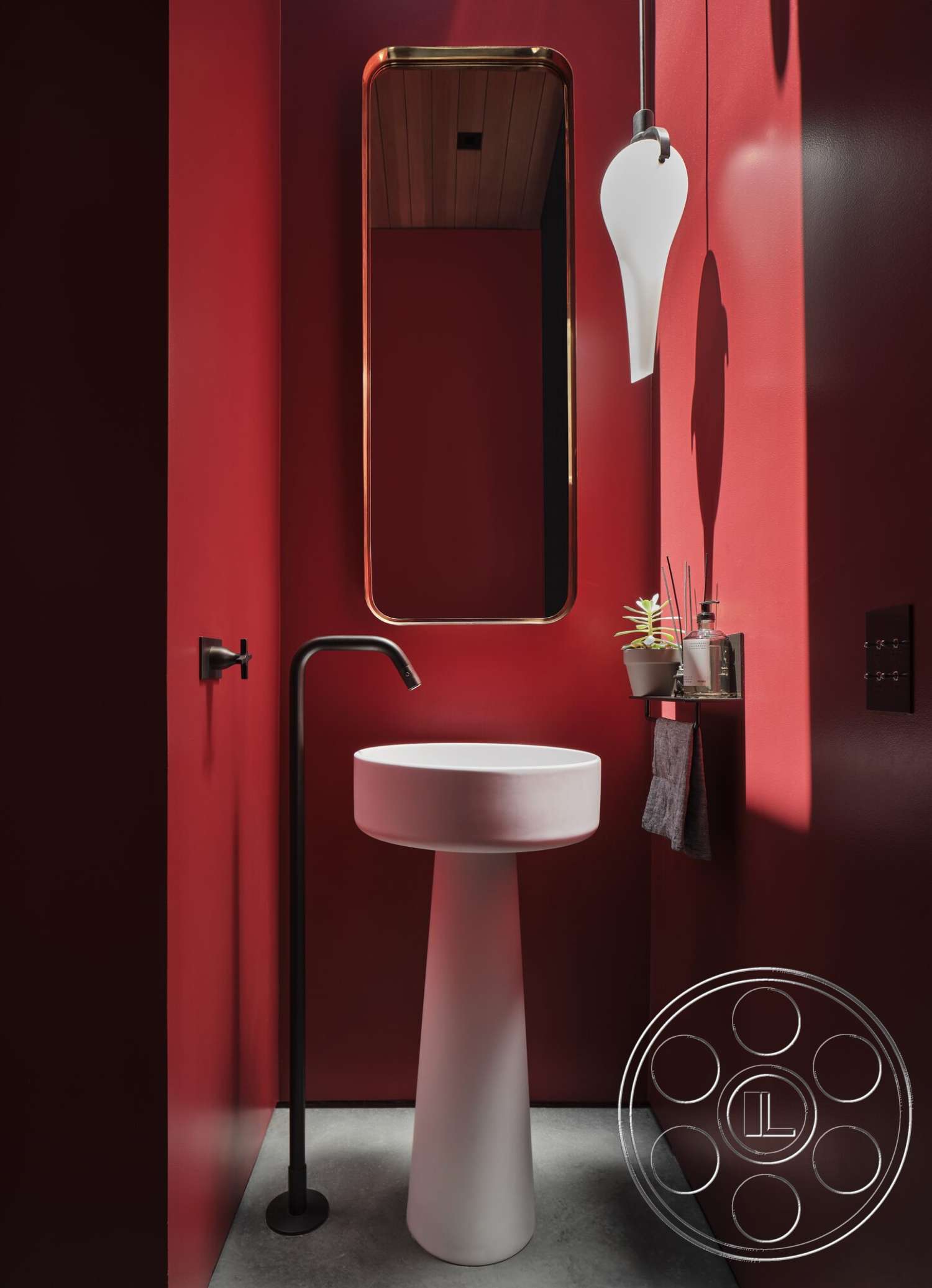 Palm Springs 110 - minimalist decor, black faucet, concrete flooring, industrial design elements, pedestal sink, greenery accent, red painted walls, gold-framed mirror, wood ceiling slats, modern pendant light, slim wall-mounted shelf