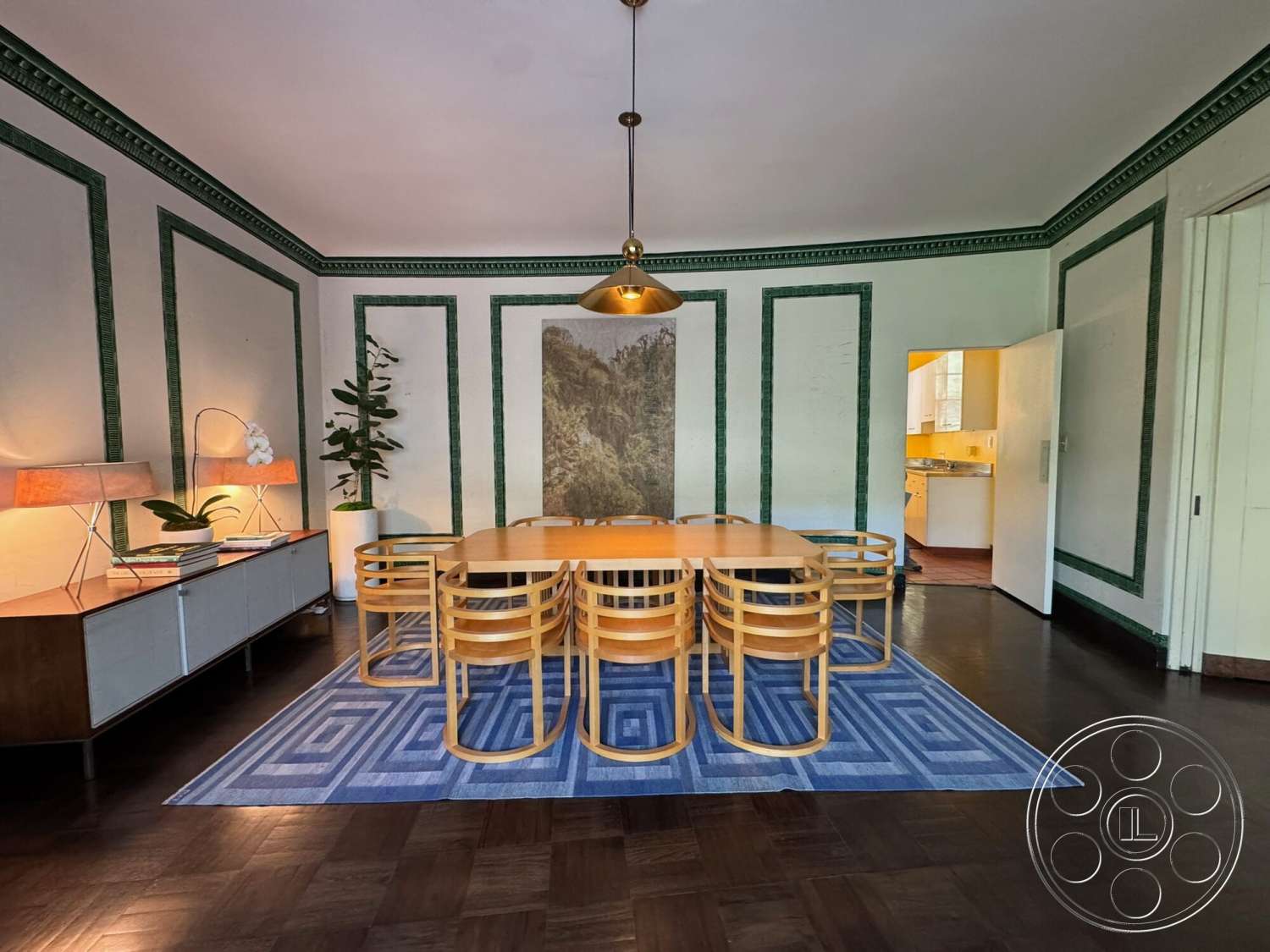 The Hearst House - floor-to-ceiling windows, decorative wall art, textured plaster walls, rectangular dining table, wooden dining chairs, modern pendant light fixture, white painted walls, crown molding details, hardwood dining room floors, geometric patterned area rug, green accent wall framing, mid-century modern sideboard, indoor plant arrangement, opens to kitchen area