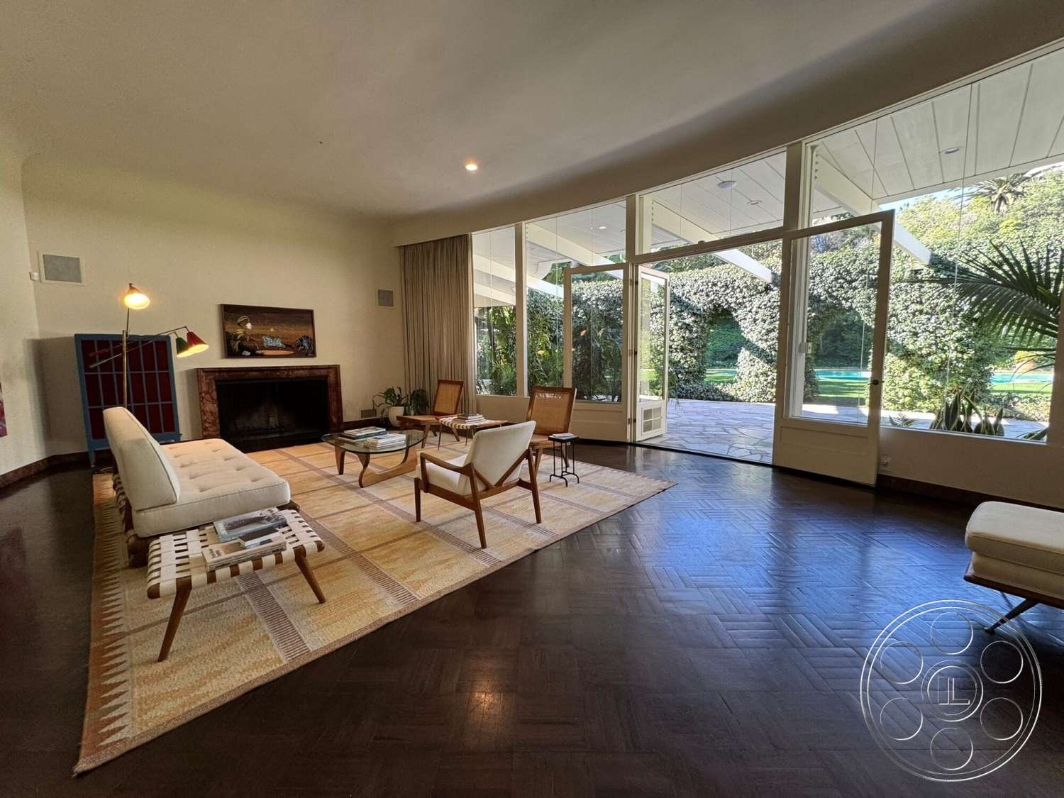 The Hearst House - white walls, natural light, stone fireplace, textured area rug, open floor plan, floor-to-ceiling windows, mid-century modern design, hardwood floor with herringbone pattern, modern armchairs