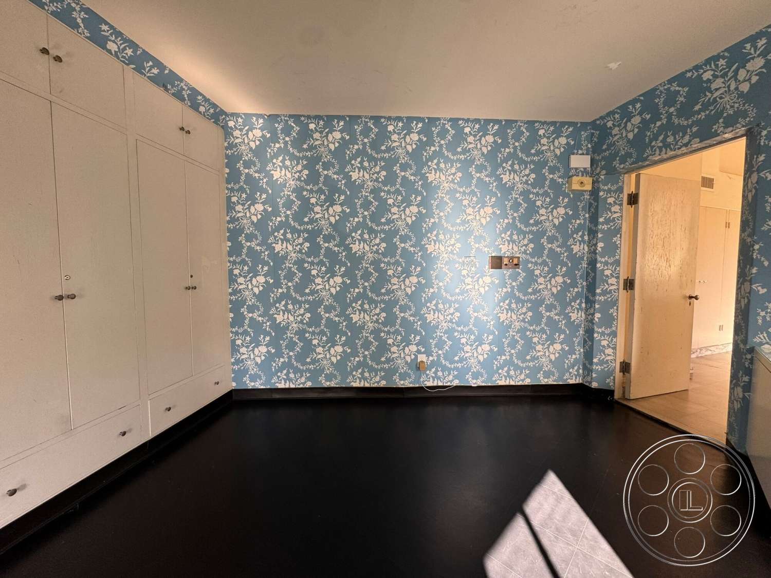 The Hearst House - neutral wall color, plain white door, light blue floral wallpaper, white built-in cabinets, black vinyl flooring, neutral lighting, corner doorframe, simple hardware details