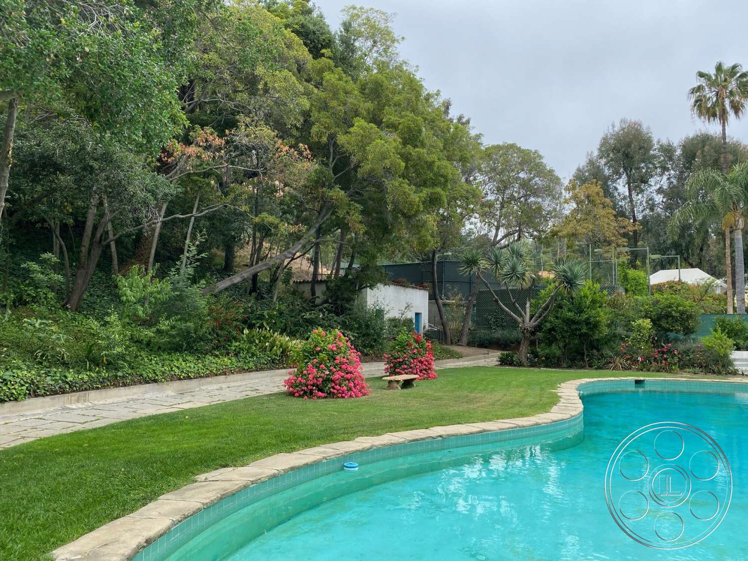 The Hearst House - exterior, curved pathway, fenced garden area, tall trees, tropical landscaping, green grass lawn, lush garden setting, stone patio flooring, concrete pool border, decorative flower beds, kidney-shaped pool