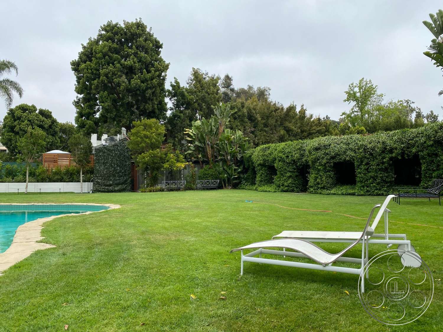 The Hearst House - exterior, brick patio, lawn area, tropical landscaping, garden setting, white lounge chairs, shade trees, rectangular pool, concrete pool border, green hedge wall, pathway around pool