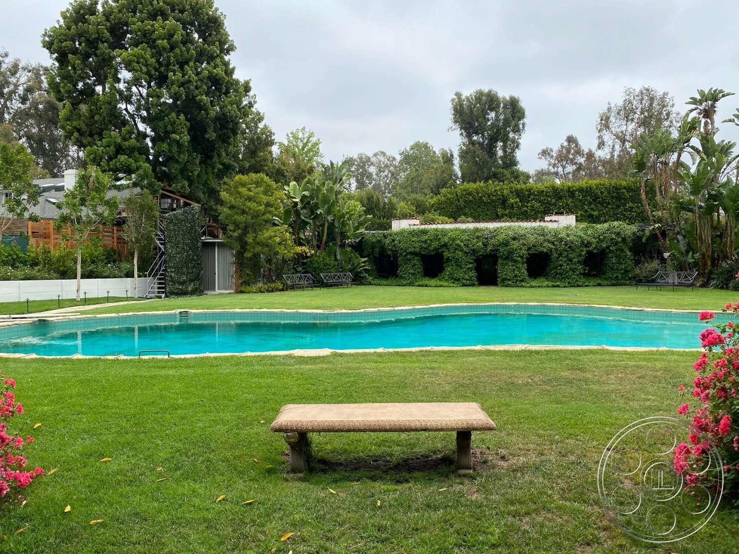 The Hearst House - exterior, lush greenery, tropical plants, modern landscaping, grass lawn, garden patio, rectangular pool, two-story house, natural stone textures, stone edging, flowering shrubbery, wooden garden bench, concrete pool border, scenic garden setting, metal outdoor staircase