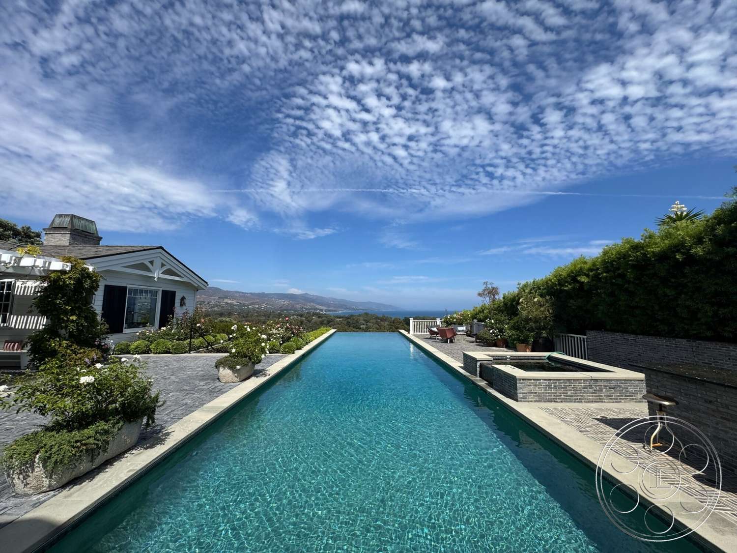 Americana 113 - exterior, glass sliding doors, outdoor seating area, rectangular swimming pool, city skyline view, infinity pool, slate roof, hillside location, brick pool deck, stone feature wall, modern residential architecture, white painted walls, surrounding lush greenery, stone patio flooring, concrete pool border, landscape garden with flowering plants