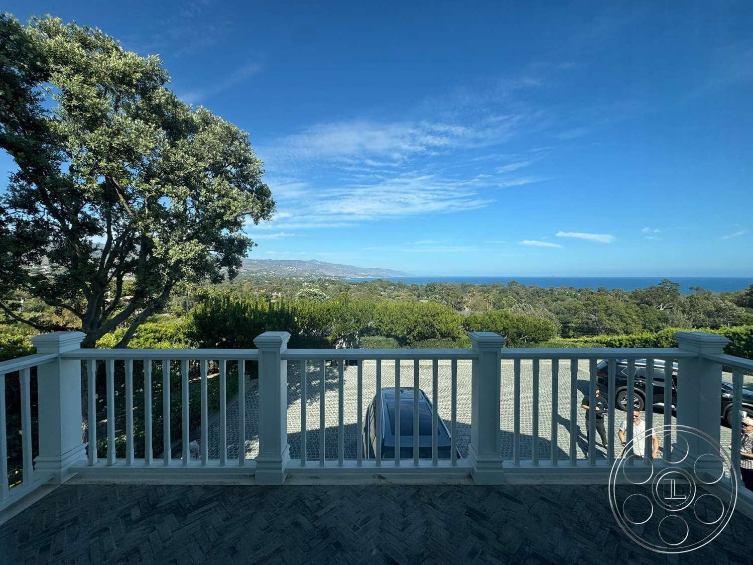 Americana 113 - exterior, paved driveway, lush greenery, ocean view, clear blue sky, hillside location, distant mountains, white wooden railing, herringbone pattern paving stones