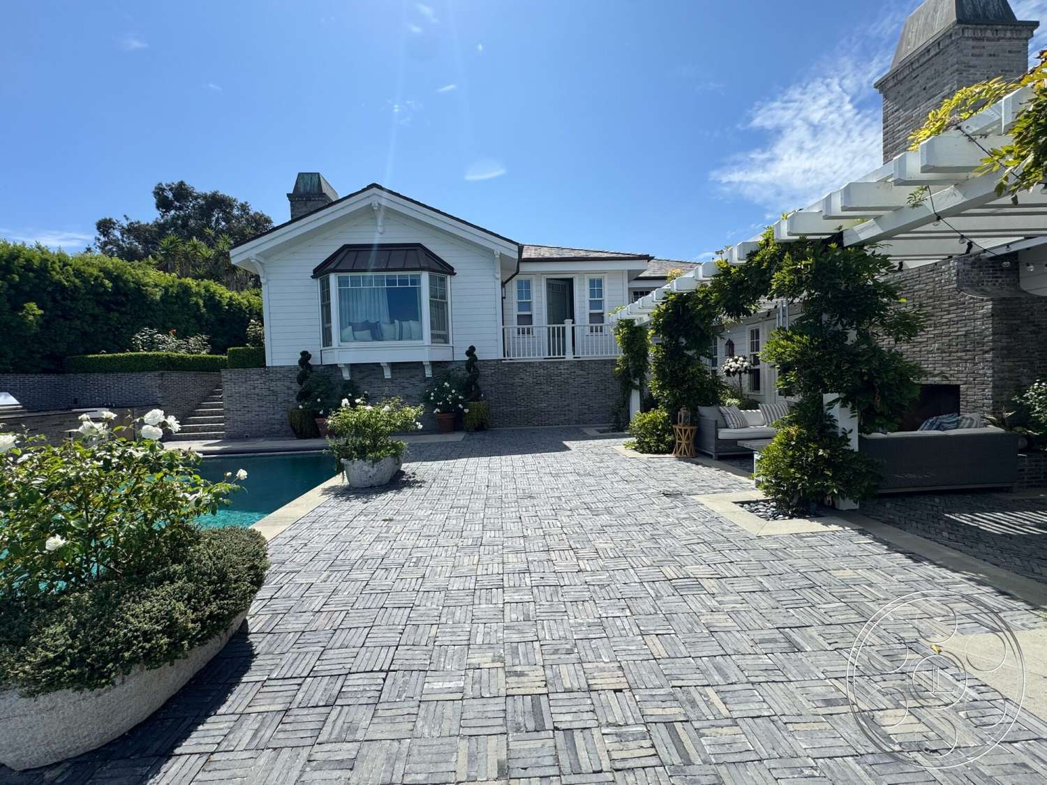 Americana 113 - large windows, exterior, outdoor seating area, decorative planters, white wood siding, exposed stone wall, cozy outdoor lounge, landscaped garden area, natural light-filled space, sloped roof design, stone patio flooring, brick paver walkway, rectangle pool shape, pergola with greenery, contemporary style home, poolside garden