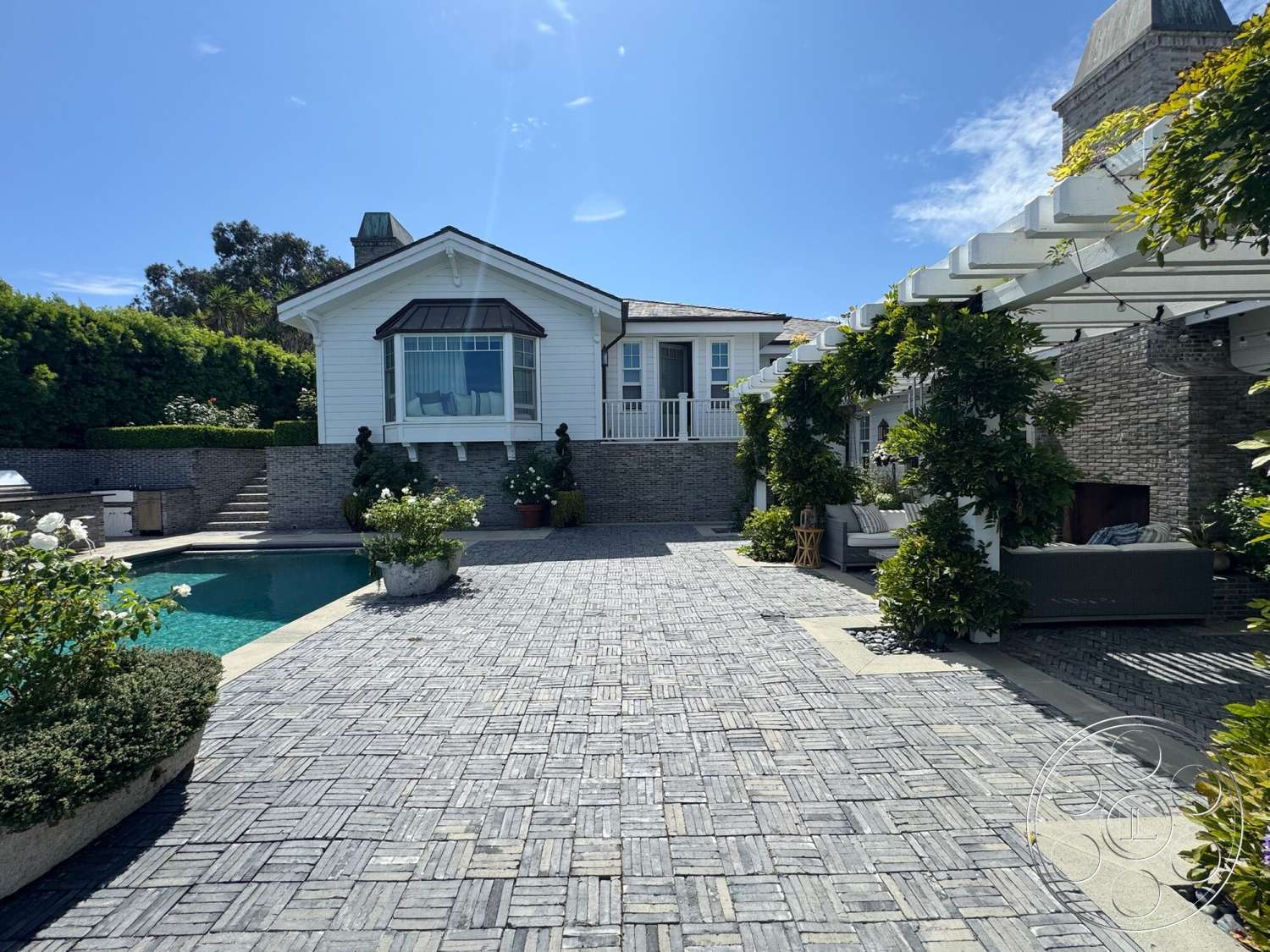Americana 113 - exterior, glass sliding doors, modern outdoor furniture, planter boxes, gabled roof, rectangular pool, exposed stone wall, landscaped garden area, white painted walls, concrete pool border, brick patio flooring, pergola with climbing plants, hardscaped terrace