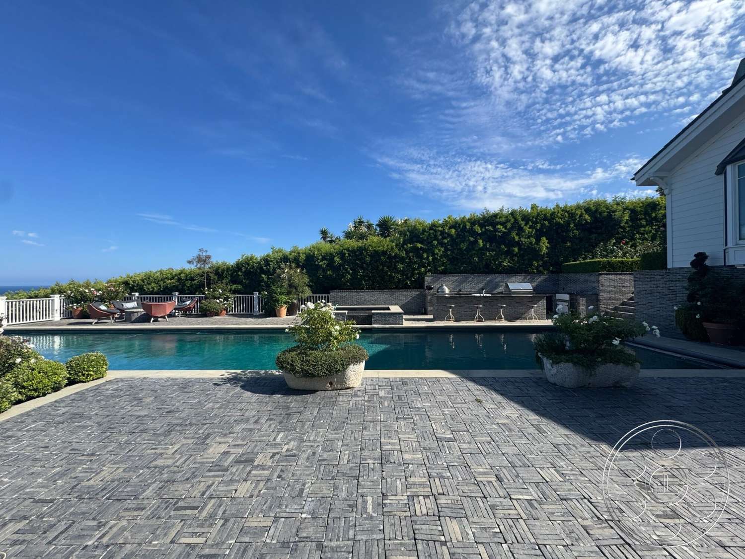 Americana 113 - exterior, potted plants, modern outdoor furniture, blue sky, rectangular pool, sunny outdoor setting, landscaped garden beds, stone patio flooring, green hedge privacy wall, grey stone outdoor kitchen