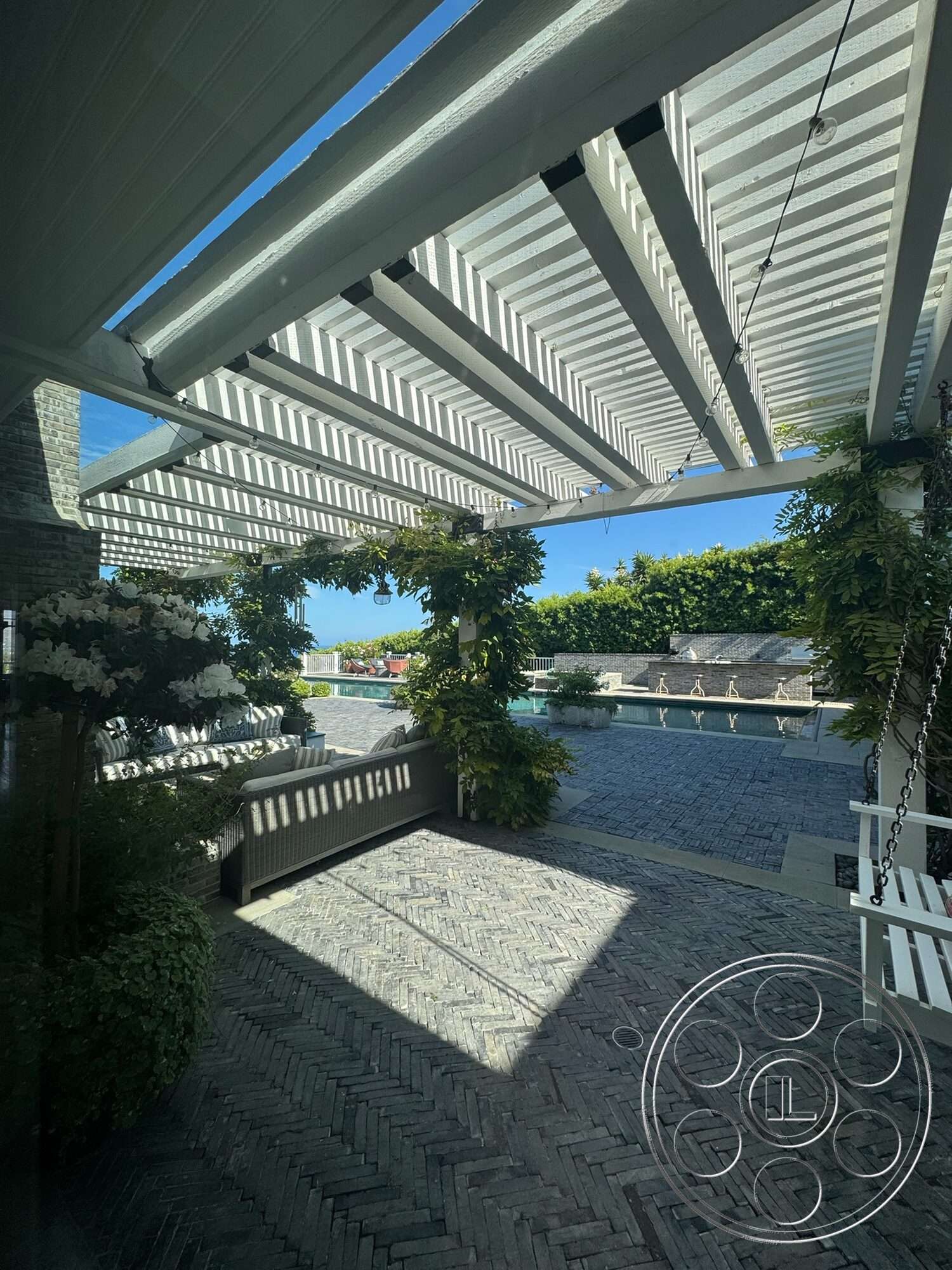 Americana 113 - exterior, in-ground swimming pool, decorative outdoor lighting, modern outdoor seating, lush greenery landscaping, sunny garden patio, wood pergola roof, herringbone stone patio flooring