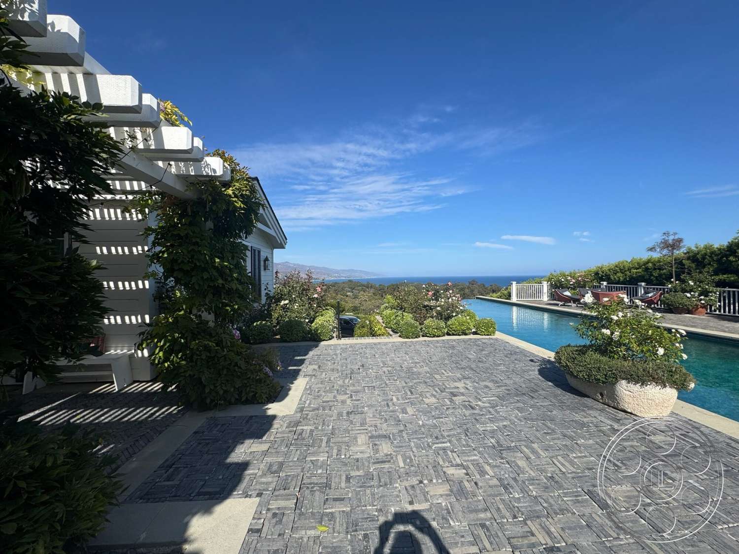 Americana 113 - exterior, ocean view, rectangular pool, stone pool deck, concrete pool coping, lush greenery landscaping, paver patio flooring, blue sky backdrop, white wooden pergola, bordered garden beds