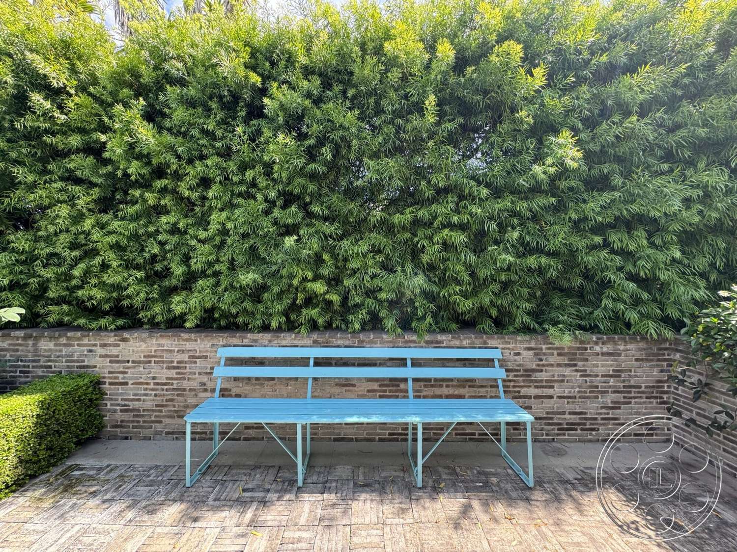 Americana 113 - exterior, lush green hedges, landscaped garden setting, brick garden wall, paved patio flooring, blue metal bench