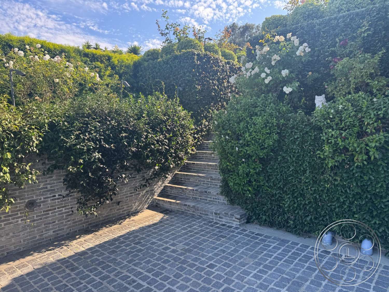 Americana 113 - exterior, brick wall, flowering shrubs, landscape lighting, stone steps, natural stone retaining wall, dense greenery, cobblestone patio floor, sloped hill