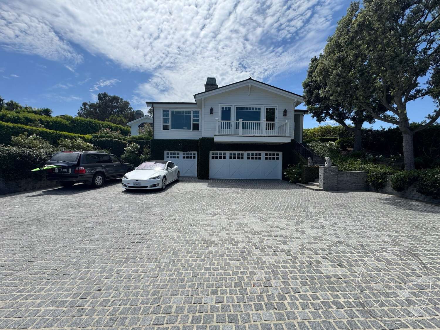 Americana 113 - large windows, exterior, asphalt shingle roof, paver driveway, balcony with railing, gabled roof, decorative stone planters, two-story home, landscaped garden beds, stone retaining walls, covered porch area, white vinyl siding, hedge privacy screens, front entry steps