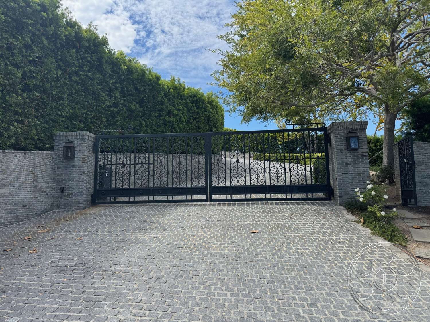 Americana 113 - exterior, lush greenery, stone pavers, modern architectural style, cobblestone driveway, landscaped hedges, wrought iron gate, textured brick wall, brick gate pillars