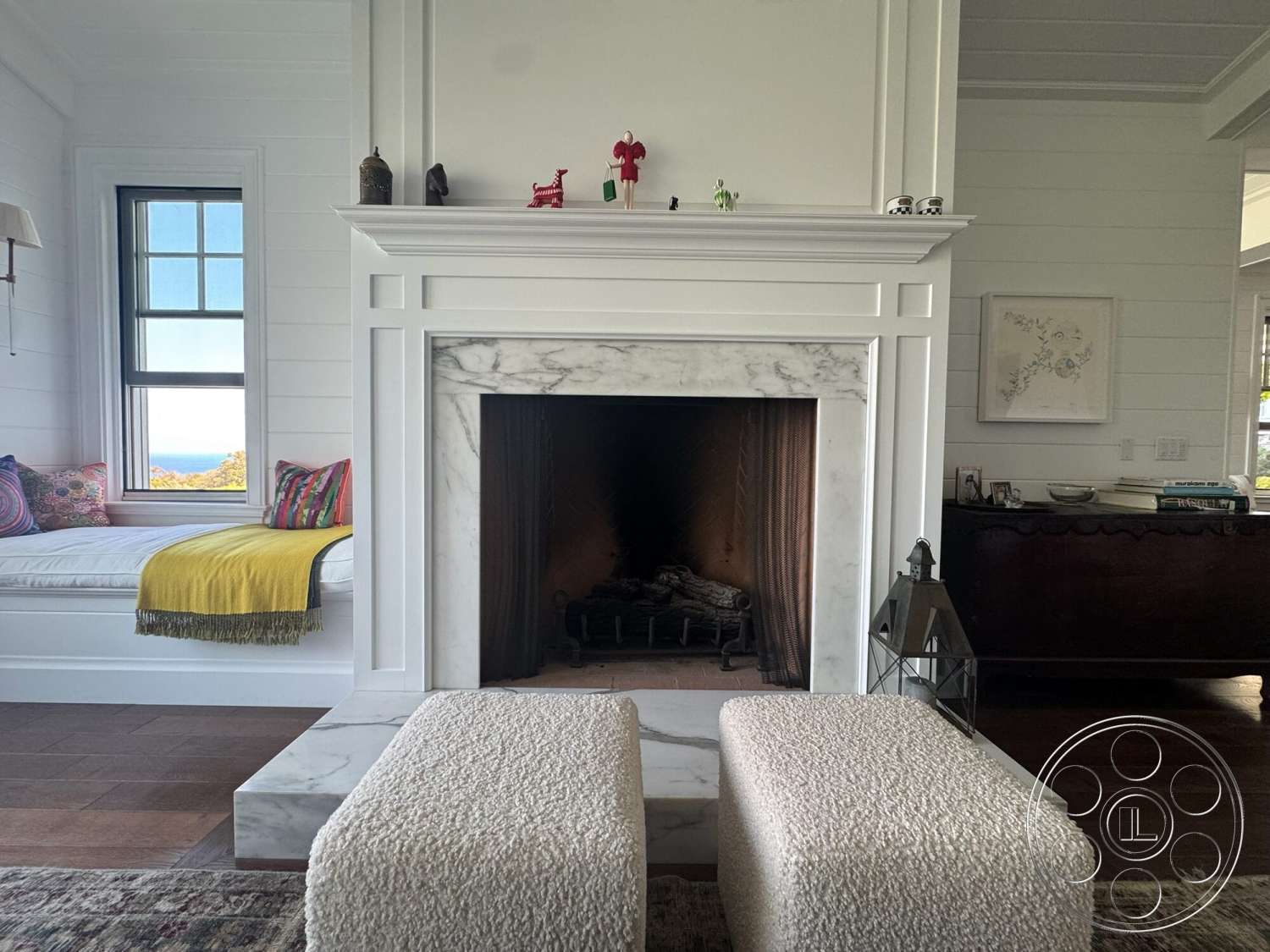 Americana 113 - vaulted ceiling, white shiplap walls, cozy reading nook, colorful throw blanket, hardwood living room floors, marble fireplace surround, traditional furniture style, large double-hung windows, built-in window seat with cushions, decorative mantel accessories, metal lantern accent