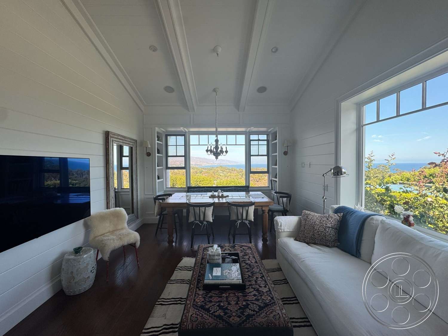 Americana 113 - white upholstered sofa, large floor-to-ceiling windows, decorative throw pillows, dark hardwood floors, area rug with geometric pattern, traditional chandelier, wood beam ceiling, framed wall mirror, rectangle dining table, modern accent chair, shiplap accent walls, built-in window seats, contemporary accent table