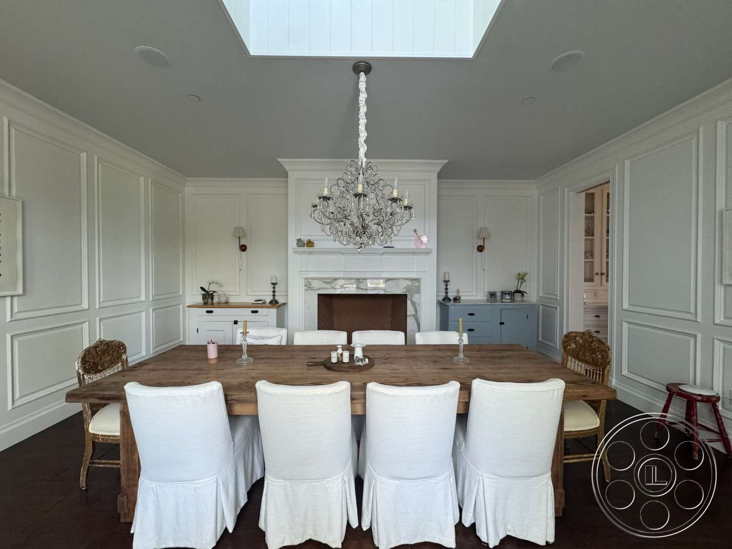 Americana 113 - neutral color palette, coffered ceiling, upholstered dining chairs, wood dining table, chandelier lighting, natural light from skylight, exposed brick fireplace surround, built-in kitchen cabinets, white painted walls, hardwood dining room floors, traditional dining room, paneled wall treatments