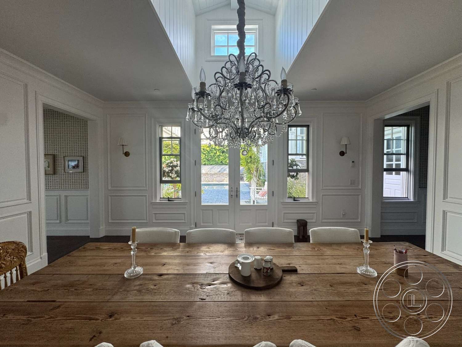 Americana 113 - natural light, dining room, elegant decor, wood dining table, open concept design, floor-to-ceiling windows, textured wall panels, hardwood floor, arched doorways, decorative wall sconces, white painted walls, chandelier lighting fixture, wainscoting wall treatment, classic upholstered chairs, rustic table centerpiece