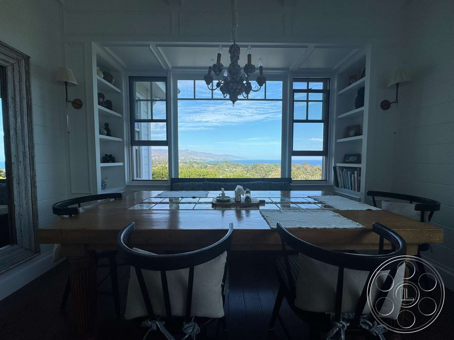 Americana 113 - natural light, wood dining table, white shiplap walls, dark hardwood flooring, textured ceiling, sea view, vintage chandelier, black wooden chairs, large bay windows, shelf built-in