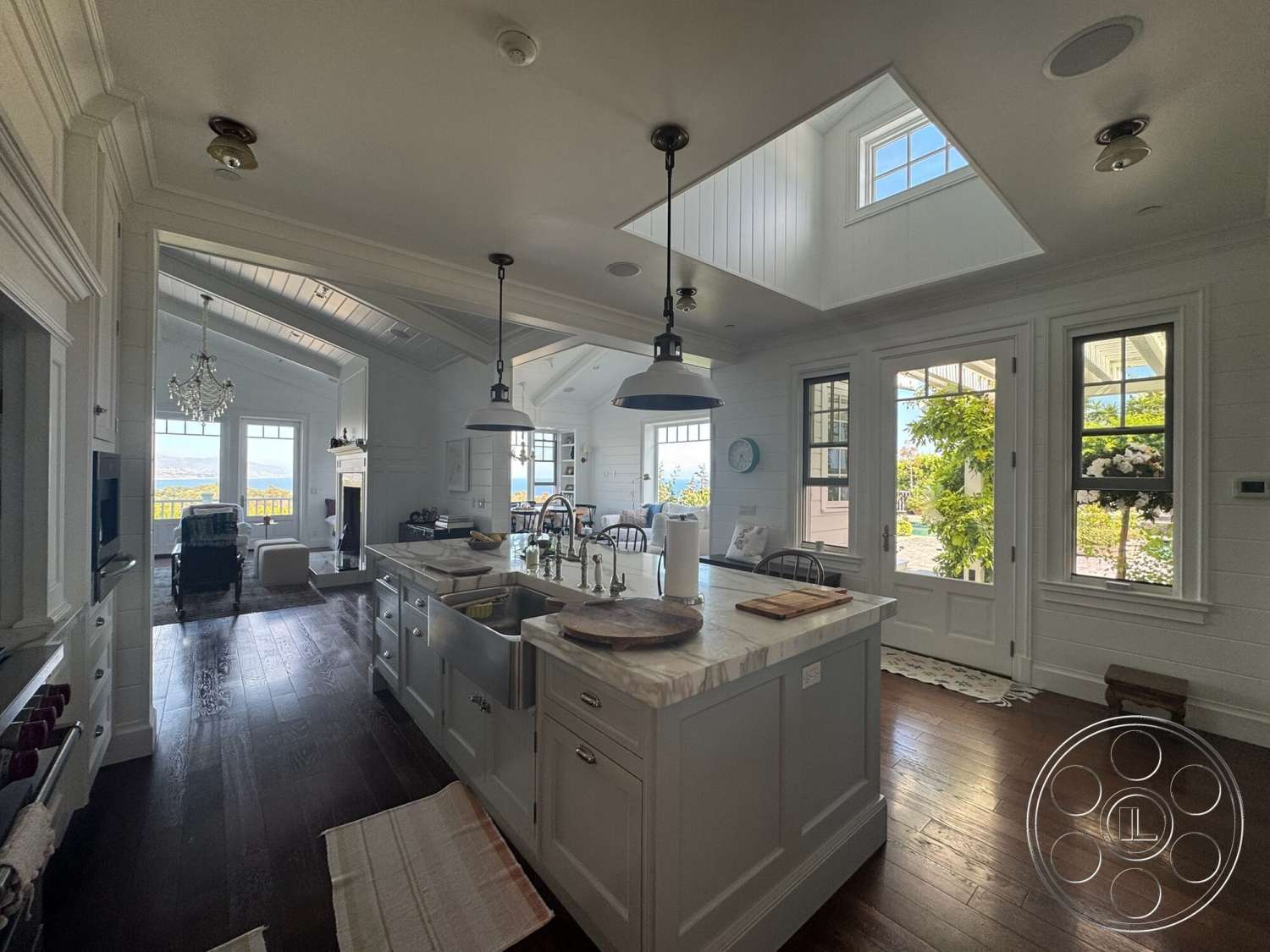 Americana 113 - open floor plan, white cabinetry, shiplap walls, marble countertop, elegant chandelier, window trim, hardwood kitchen floors, island kitchen design, crown molding details, large windows with views, farmhouse-style kitchen, vaulted ceiling with wood beams, chrome pendant lighting, stylish modern appliances