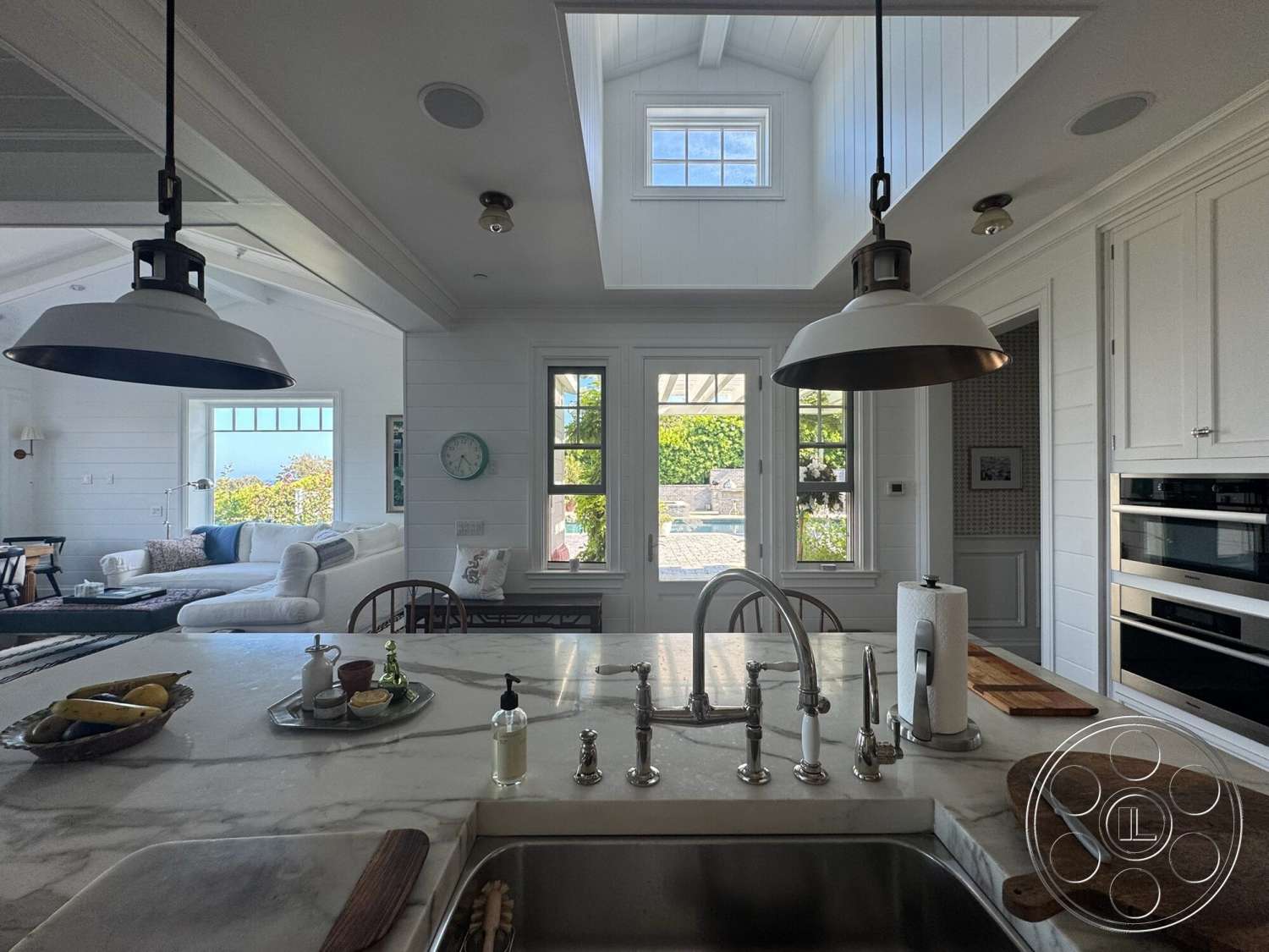 Americana 113 - hardwood flooring, open floor plan, white cabinetry, vaulted ceiling, white shiplap walls, modern farmhouse style, double-hung windows, pendant lighting fixtures, light-filled space, stainless steel kitchen appliances, marble kitchen countertops, wooden beam details, glass doors leading to outdoor patio, farmhouse kitchen sink