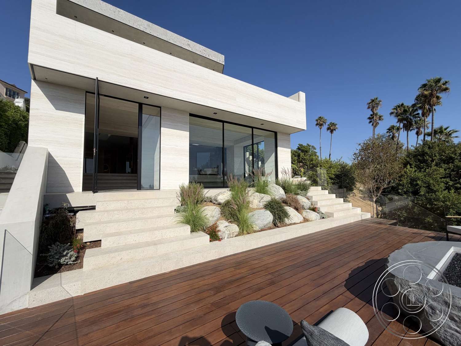 Modern 532 - exterior, glass railings, floor-to-ceiling windows, modern architectural style, staircase with stone steps, light-colored stone facade, flat roof design, wood deck flooring, palm tree surroundings, linear garden beds, concrete retaining walls, landscaped garden with rocks