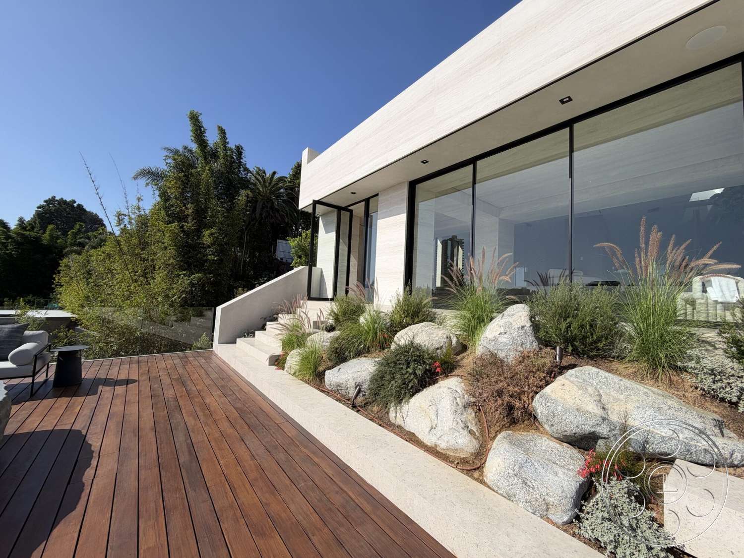 Modern 532 - exterior, horizontal siding, minimalist aesthetic, large glass windows, modern architectural style, sunny outdoor setting, natural stone boulders, wood deck flooring, low-maintenance greenery, concrete step pathway, landscaped stone garden