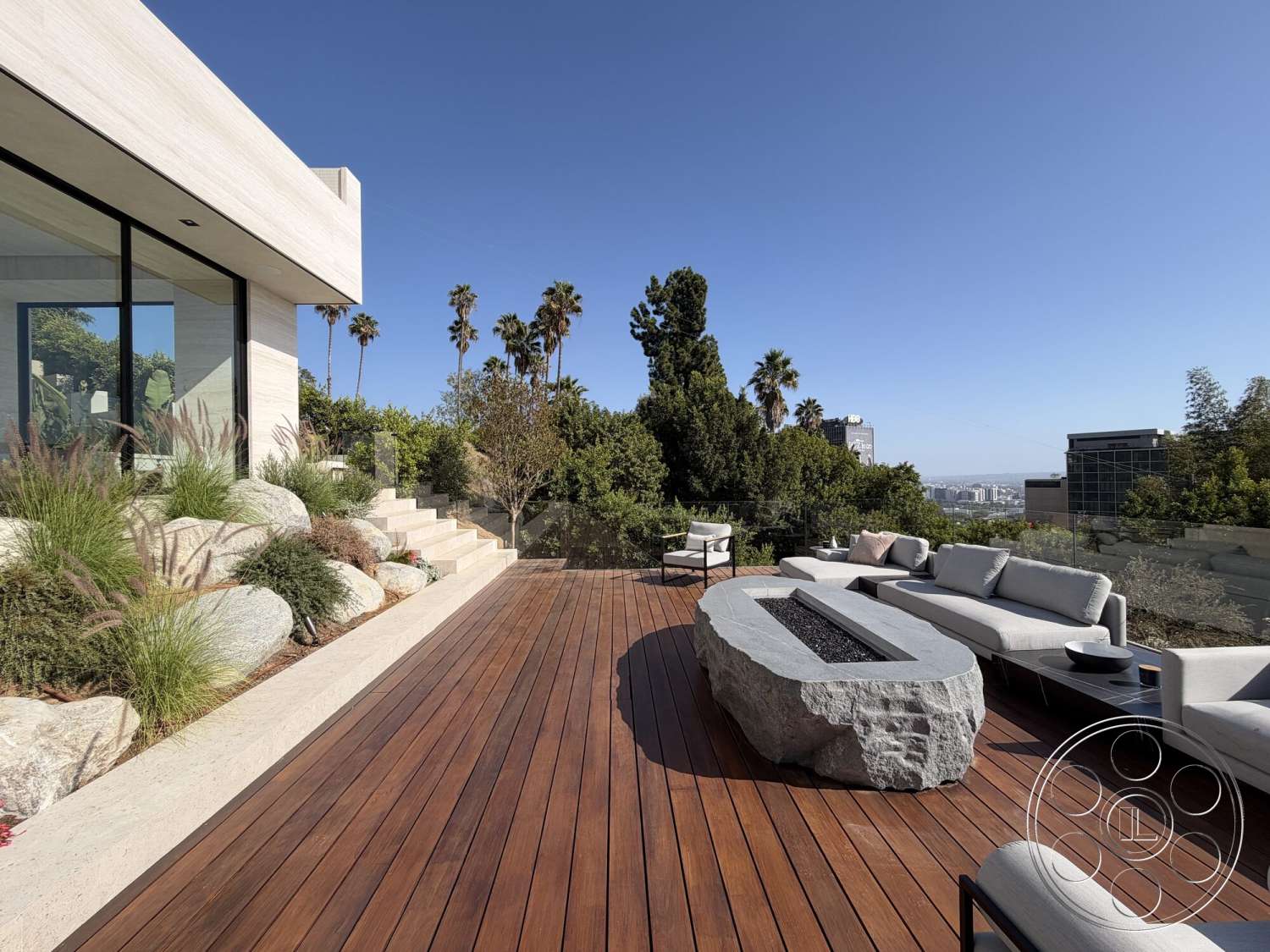 Modern 532 - exterior, landscaped garden, low-maintenance plants, glass railing, palm tree view, modern outdoor seating area, wood deck flooring, city skyline backdrop, rectangular fire pit, natural stone fire pit surround, concrete retaining wall steps