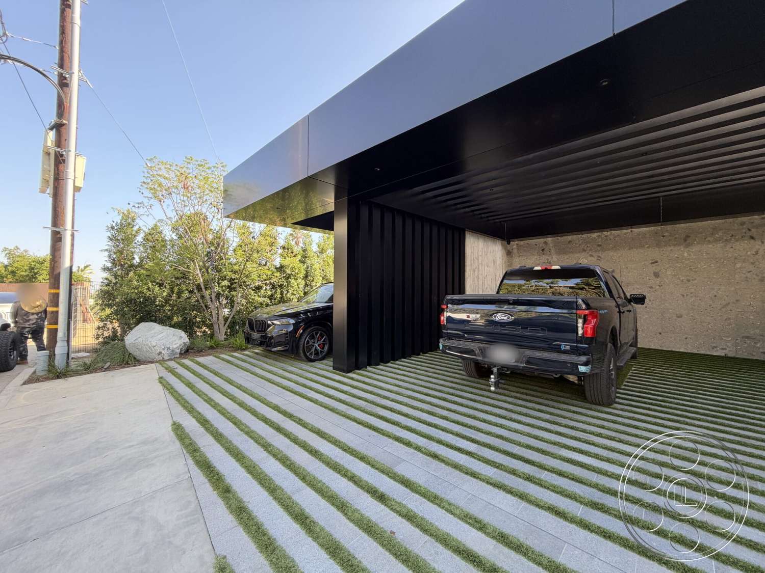 Modern 532 - exterior, flat roof, minimalist design, exposed concrete wall, concrete driveway, sloped driveway, black metal roof, landscaped garden area, vertical wood slat wall, grass pavers, modern carport