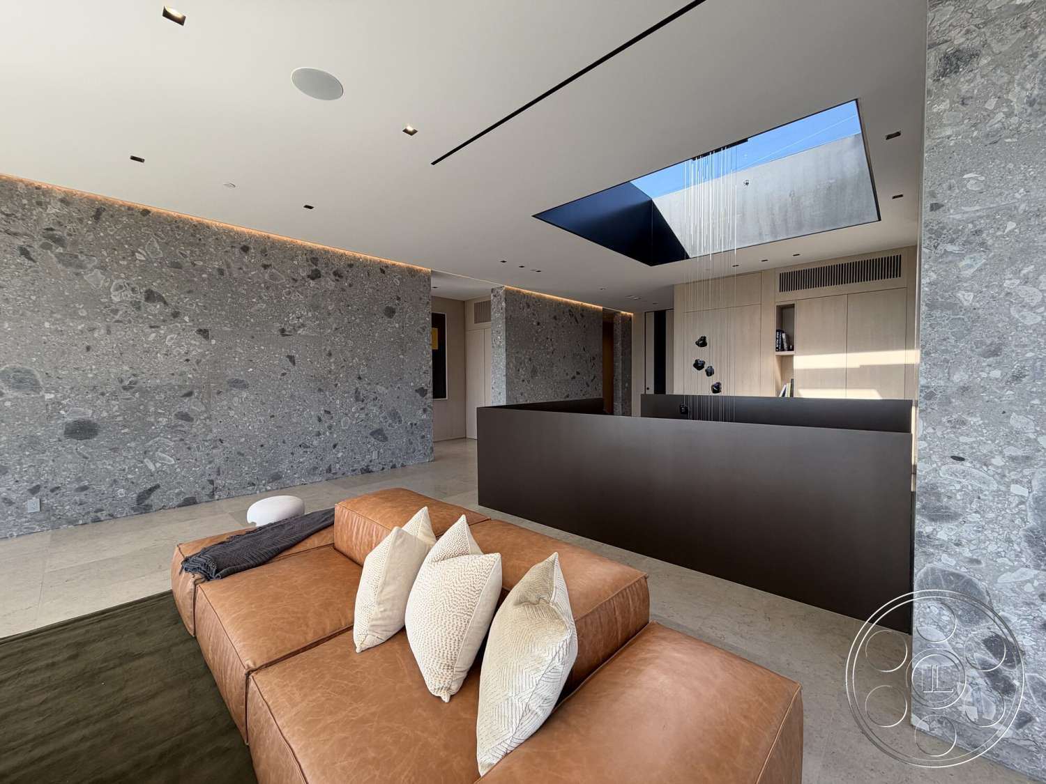 Modern 532 - neutral color palette, minimalist aesthetic, open living space, flat ceiling with recessed lighting, skylight feature, textured floor tiles, exposed aggregate stone wall, sleek wood cabinetry, tan leather sectional sofa
