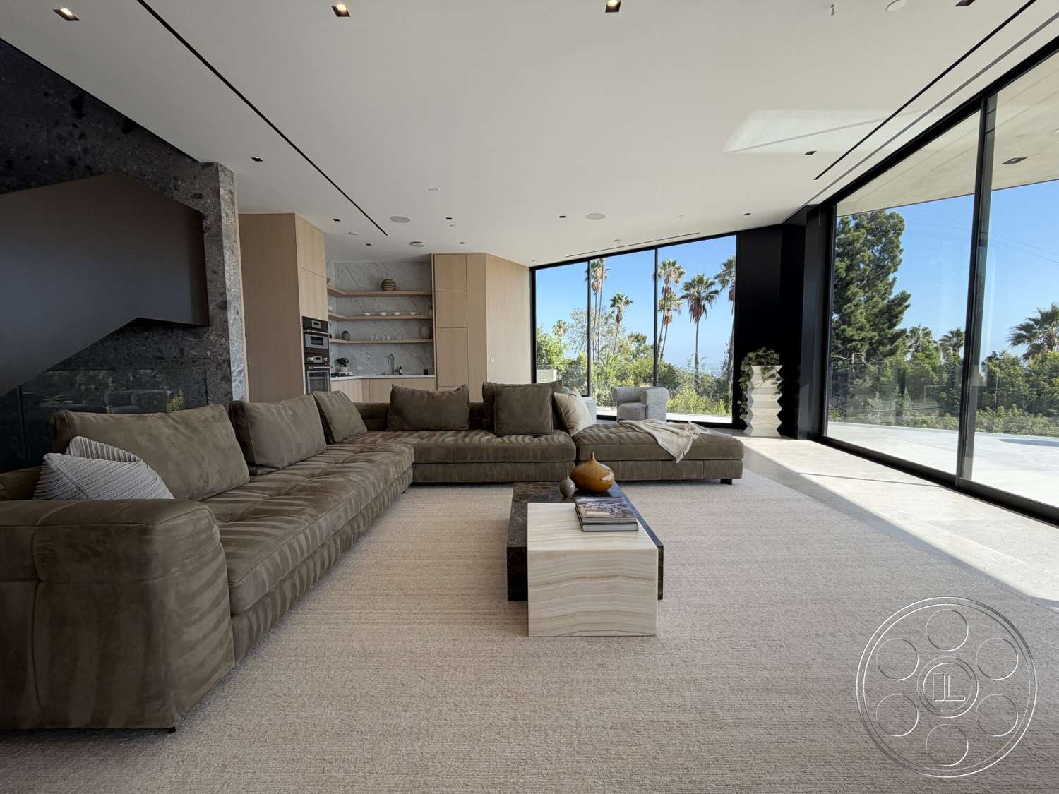 Modern 532 - natural light, wood cabinetry, luxury living room, minimalist coffee table, large sectional sofa, palm tree view, textured carpet flooring, floor-to-ceiling glass windows, dark stone accent wall, light-colored fabric upholstery, modern shelf design, lush outdoor greenery