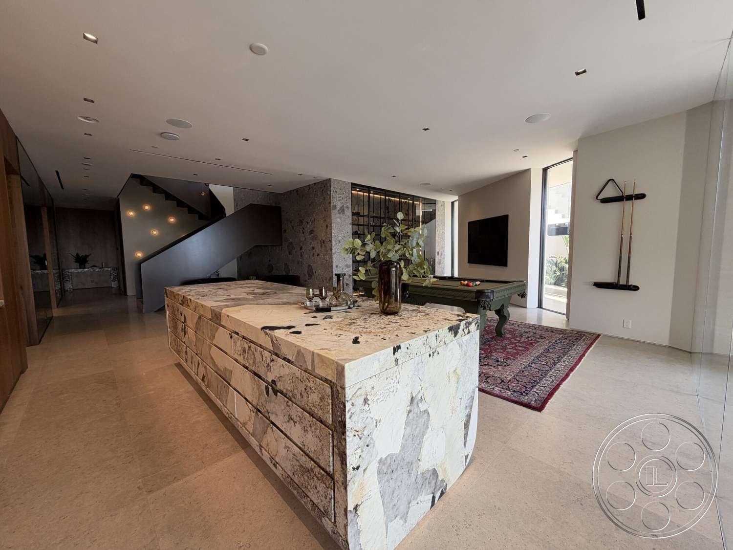 Modern 532 - neutral color palette, recessed lighting, wall-mounted television, open floor plan, minimalist design elements, large windows for natural light, decorative greenery, floating staircase, area rug with intricate pattern, glass partition wall, pool table area, natural stone kitchen island, textured light stone flooring