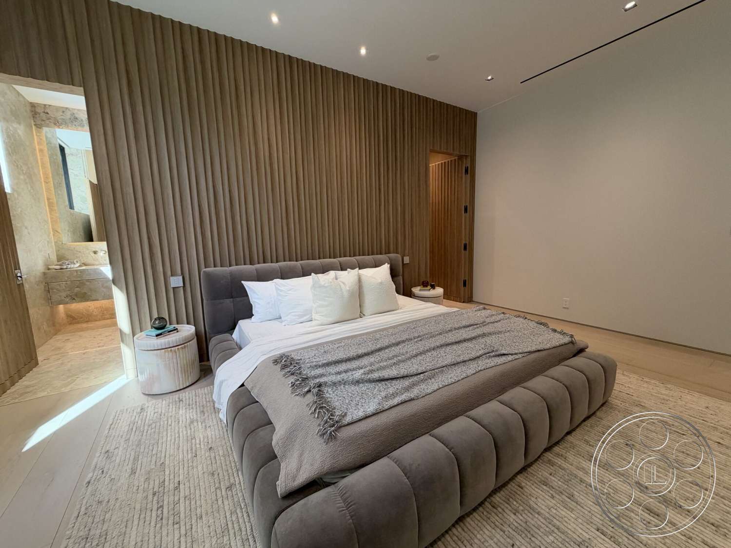 Modern 532 - neutral color palette, textured throw blanket, beige area rug, recessed ceiling lights, minimalist design aesthetic, plank hardwood flooring, open doorway to bathroom, light wood paneling wall, soft grey upholstered bed, white linen bedding, natural wood nightstand