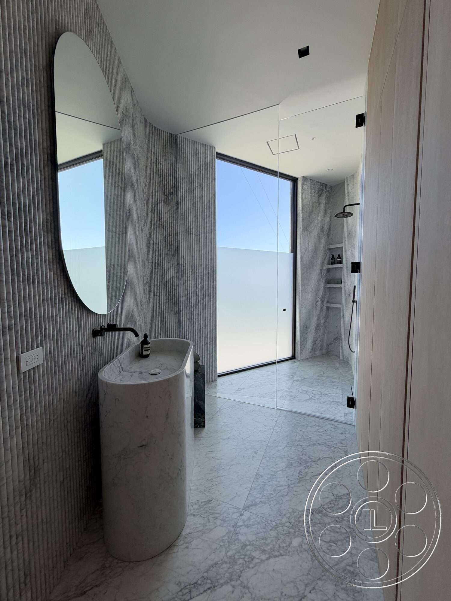 Modern 532 - glass shower enclosure, modern minimalist design, marble bathroom flooring, wood panel accent wall, large floor-to-ceiling window, black wall-mounted faucet, textured marble walls, oval marble vanity, backlit round mirror