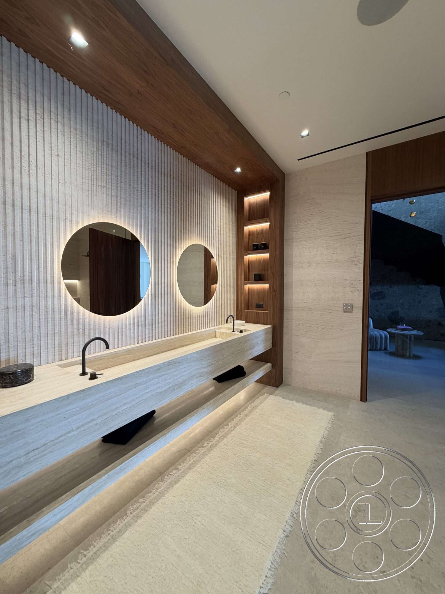 Modern 532 - neutral area rug, textured plaster bathroom walls, wood paneling accent wall, stone bathroom flooring, concrete vanity countertop, round mirrors with backlighting, linear wall-mounted lighting fixtures, floating concrete sink base, black matte faucet fixtures