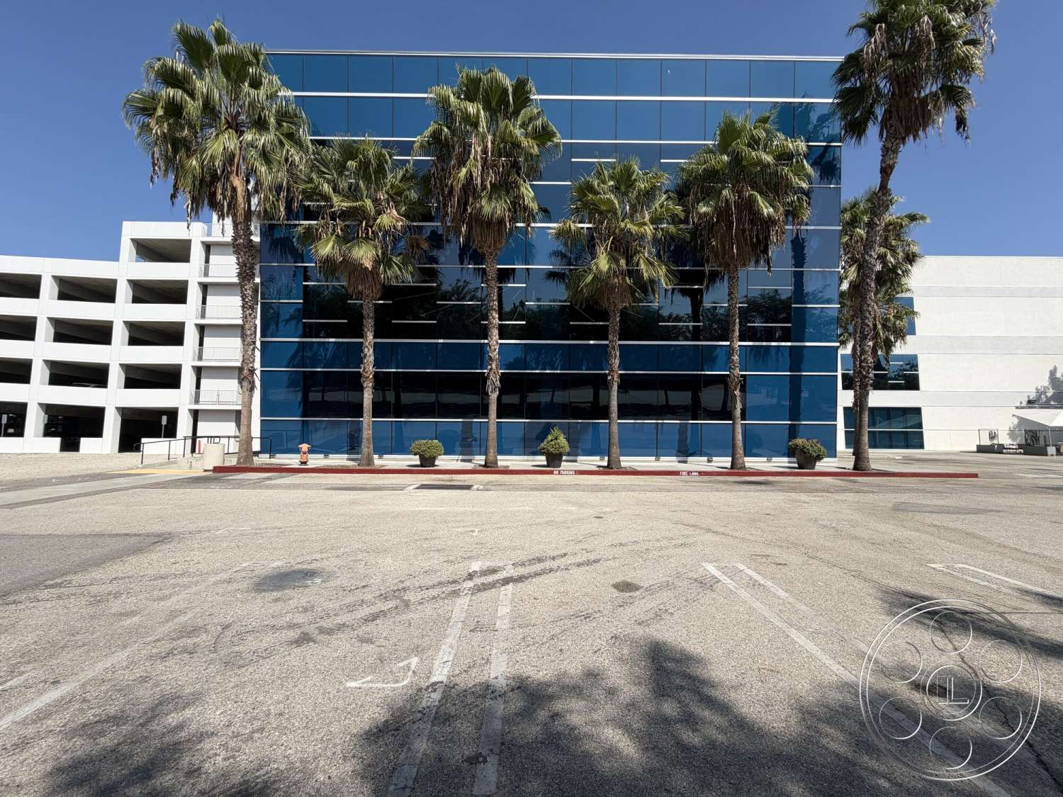 Office 130 - exterior, modern architectural style, asphalt parking lot, open parking area, concrete sidewalk, flat roof design, palm trees landscape, glass facade windows, white stucco building, red curb border, multi-story office building