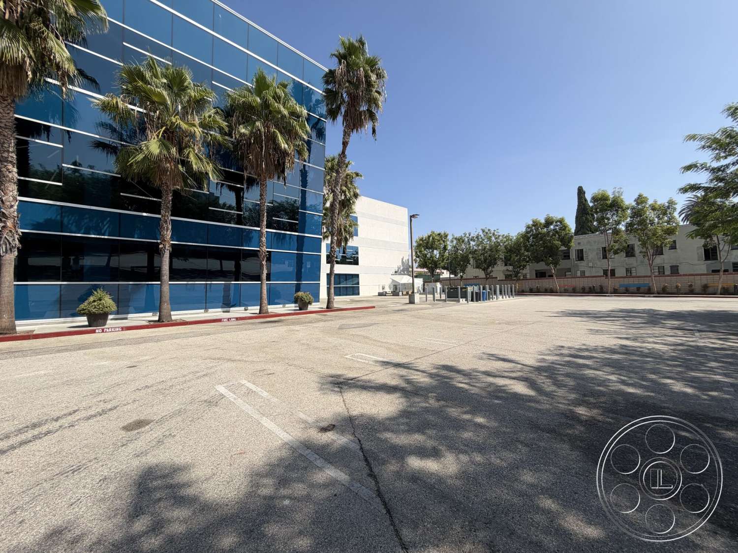 Office 130 - exterior, palm trees, urban setting, glass facade, landscaped planters, concrete parking lot, red curb, blue glass windows