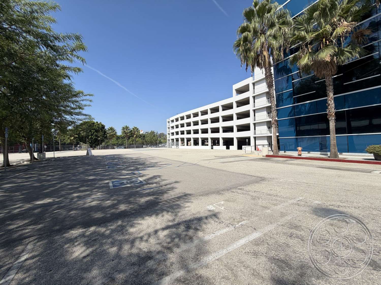 Office 130 - exterior, modern architecture, open space, urban setting, paved surface, concrete parking lot, multi-story parking garage, glass curtain wall, sunny day, landscaped palm trees