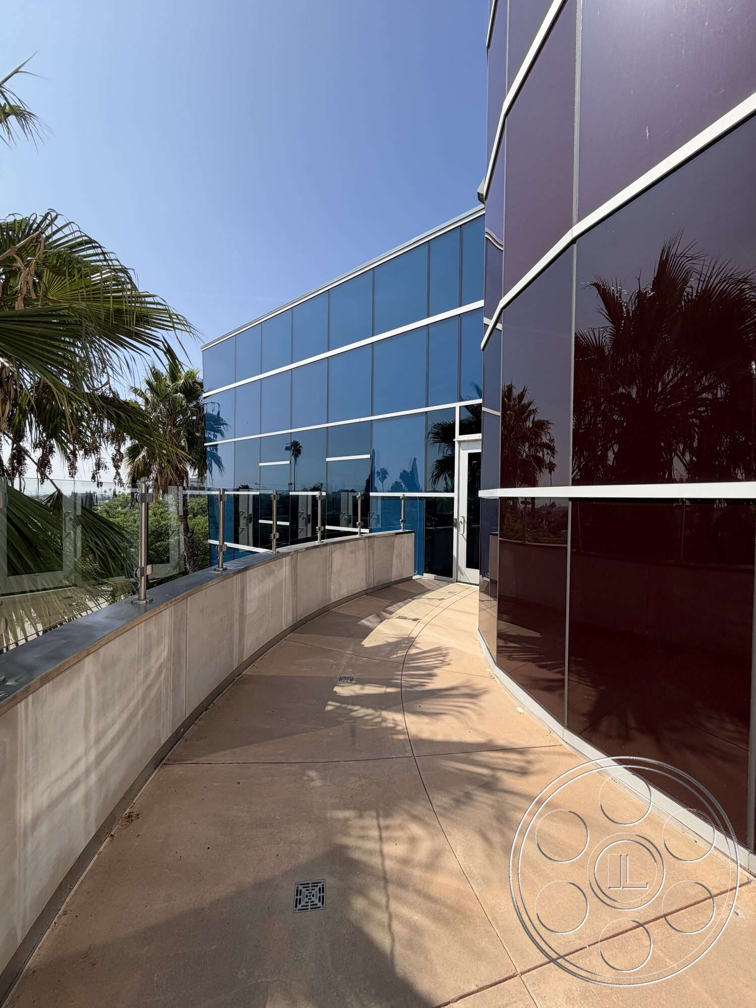 Office 130 - exterior, metal railing, floor-to-ceiling windows, glass facade, modern architectural style, tropical landscaping, steel frame construction, polished concrete surface, curved concrete walkway, palm trees surrounding the building