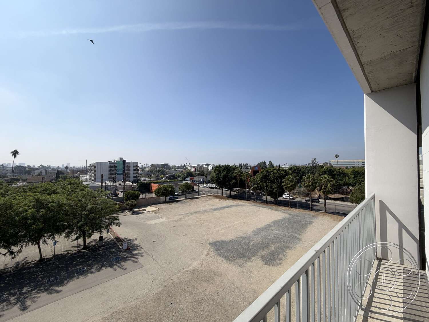 Office 130 - exterior, clear blue sky, asphalt parking lot, minimalist architectural style, urban city view, landscape with palm trees, concrete balcony railing, low-rise residential buildings, open vacant lot