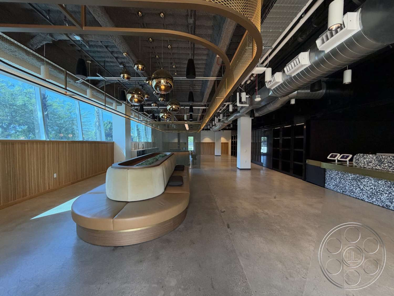 Office 130 - polished concrete flooring, modern pendant lighting, exposed ductwork, large floor-to-ceiling windows, open layout design, industrial-style architecture, natural light ambiance, curved seating area, wood panel accent wall, gold accent trim, dark feature wall, reception desk with stone top, suspended ceiling detail