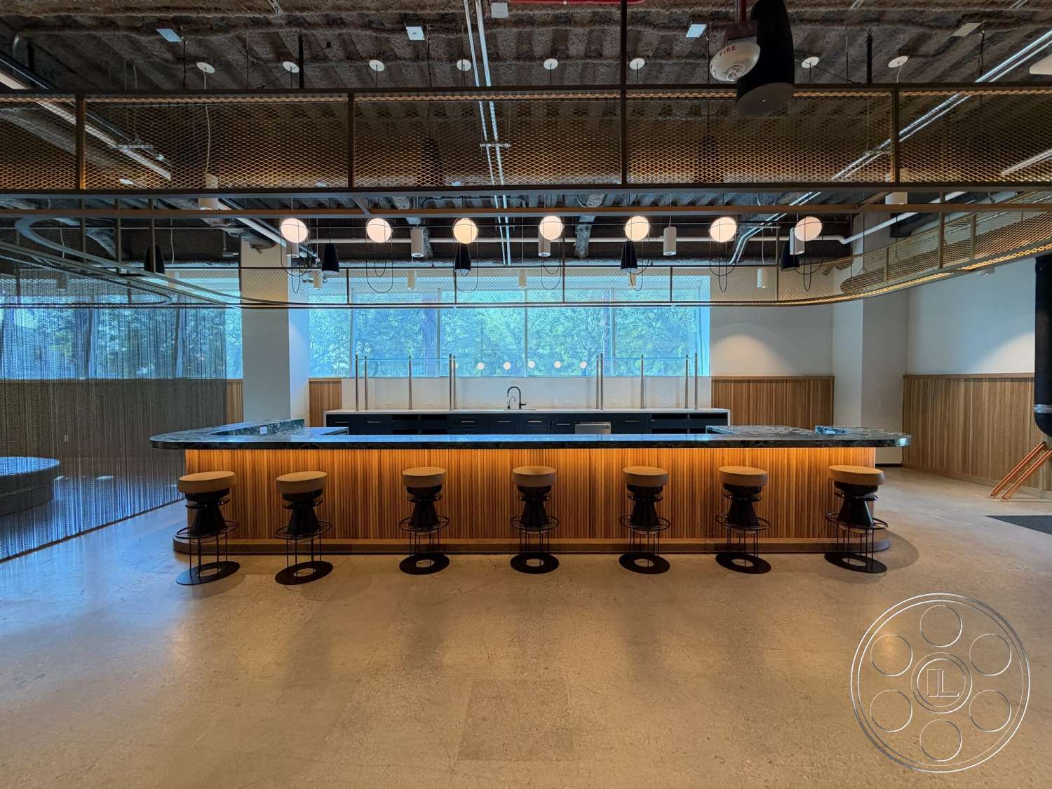 Office 130 - wood paneling, concrete flooring, large glass windows, modern design elements, ambient lighting, marble countertop, textured wall treatments, pendant lighting fixtures, exposed industrial ceiling, metal mesh partition, open bar layout, barstools with metal bases
