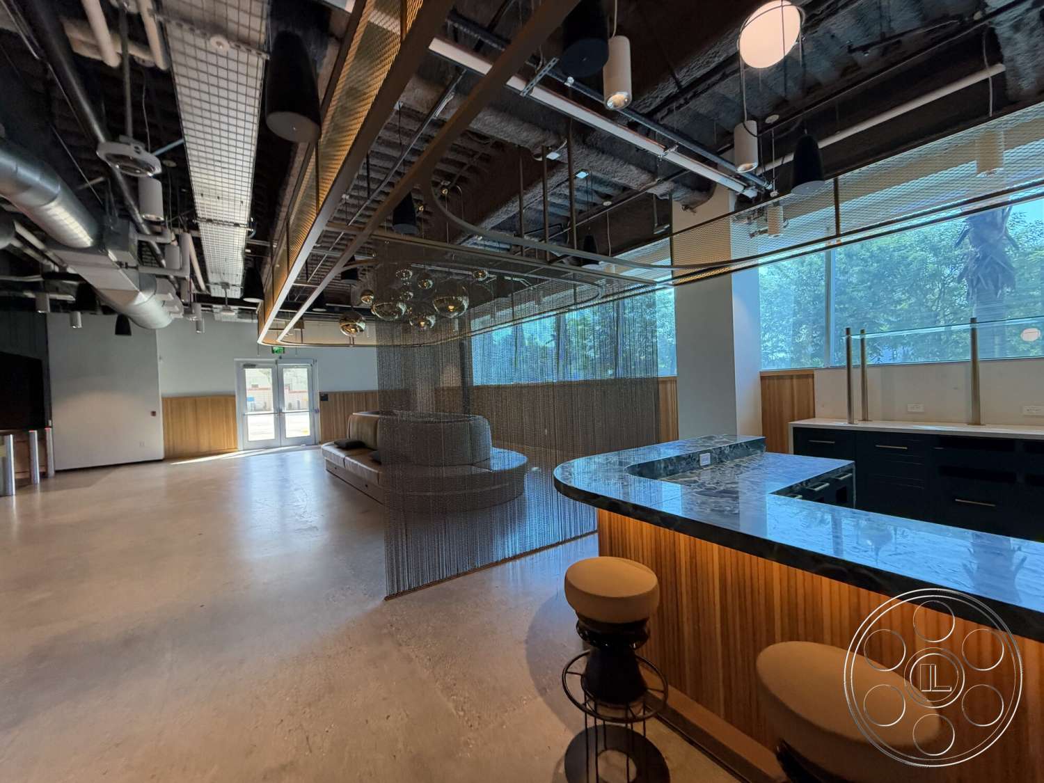 Office 130 - recessed lighting, concrete flooring, industrial style, floor-to-ceiling windows, exposed ductwork, modern bar stools, open-plan layout, marble kitchen countertop, wood panel accent wall, glass partition wall, metal suspended ceiling, circular bar area