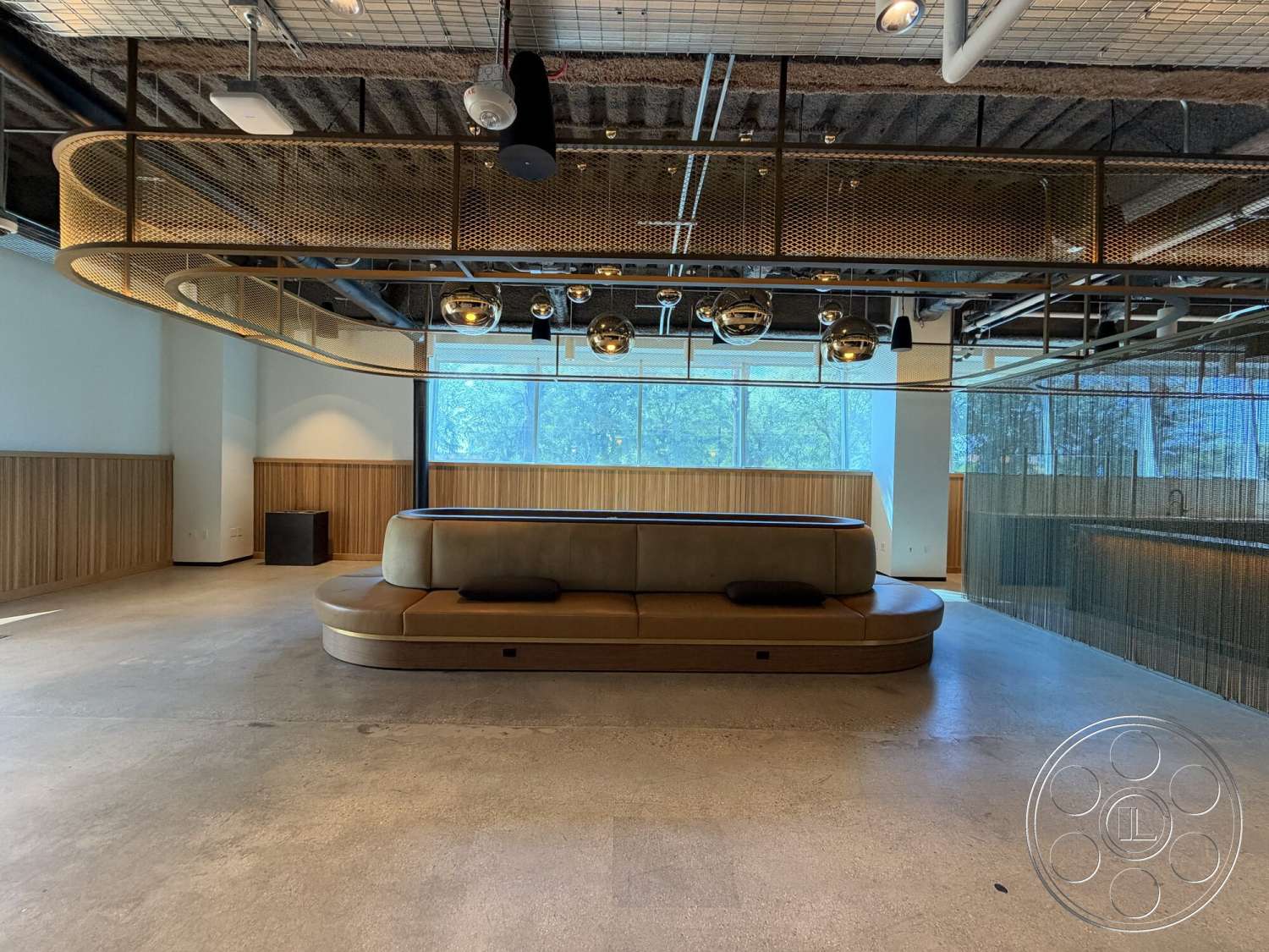 Office 130 - minimalist design, open layout, concrete flooring, industrial style, floor-to-ceiling windows, wood paneling accent wall, curved leather sofa, metal mesh ceiling fixture, glossy pendant lights