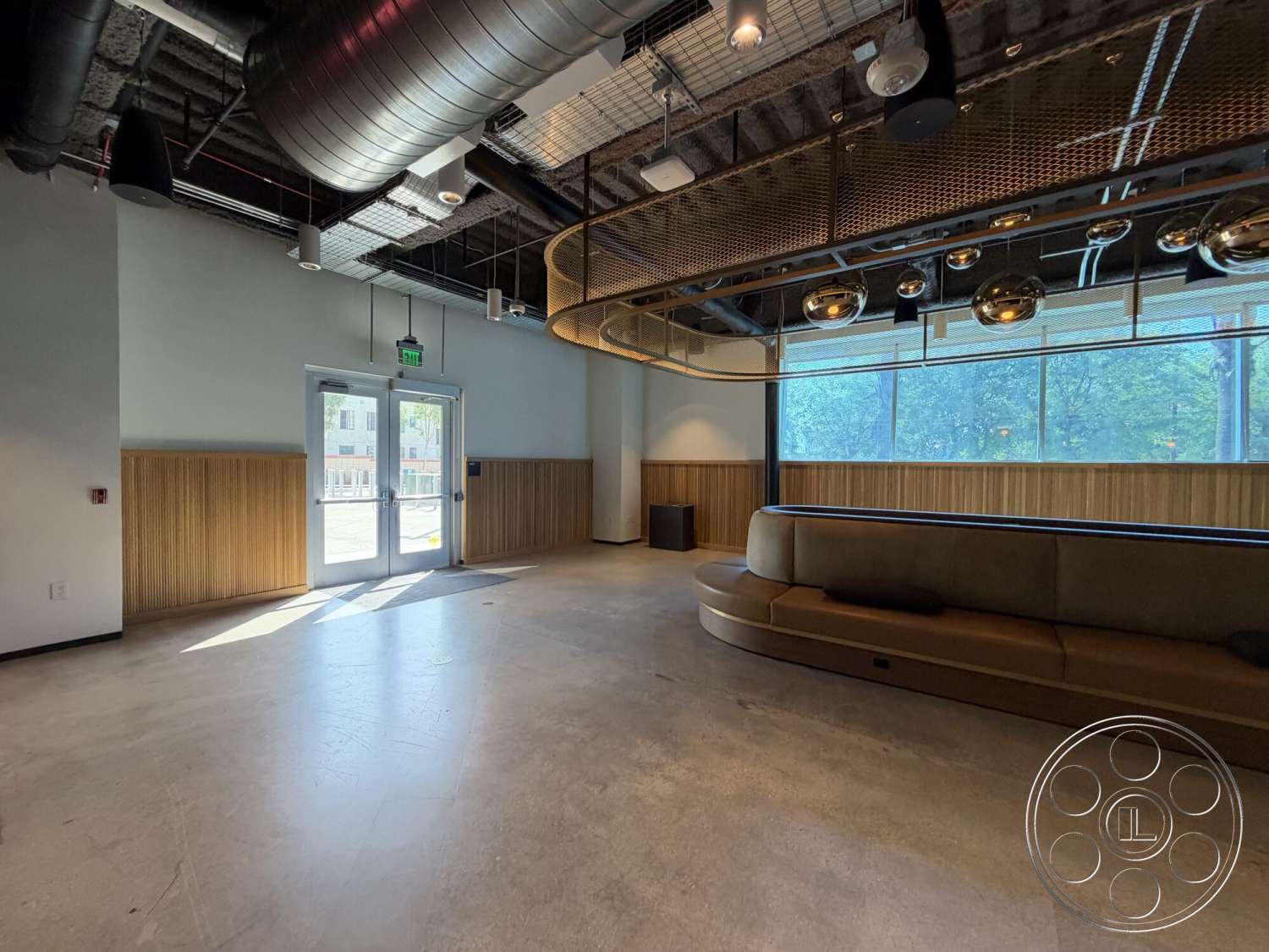 Office 130 - open floor plan, concrete flooring, floor-to-ceiling windows, curved sofa, wood panel accent walls, natural light ambiance, exposed metal ceiling beams, modern design aesthetic, round gold light fixtures