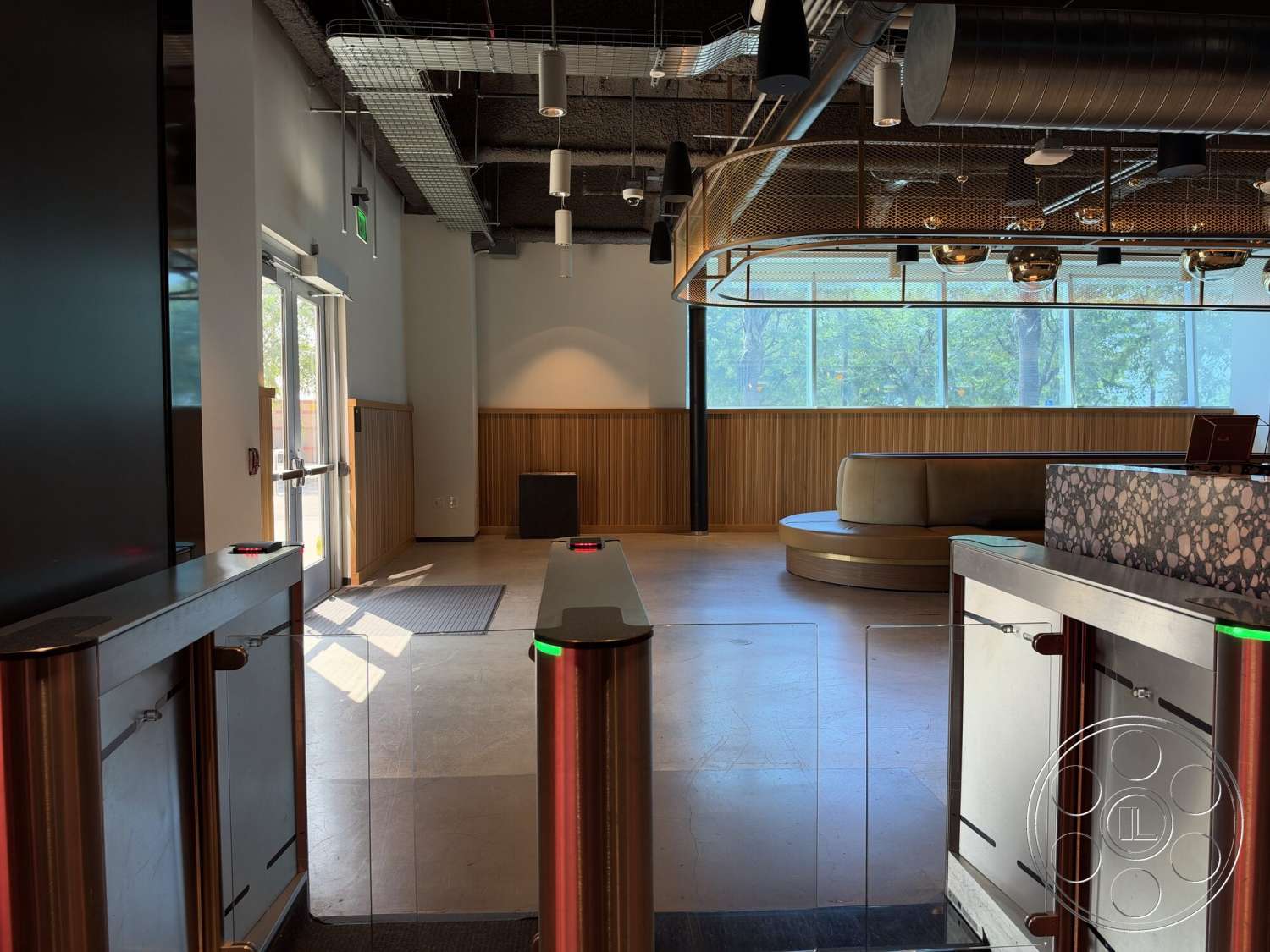 Office 130 - recessed lighting, minimalist design, polished concrete flooring, large floor-to-ceiling windows, textured wall details, curved seating area, glass entrance doors, wood panel accent wall, modern pendant lights, drop ceiling with exposed ductwork, metal security turnstiles