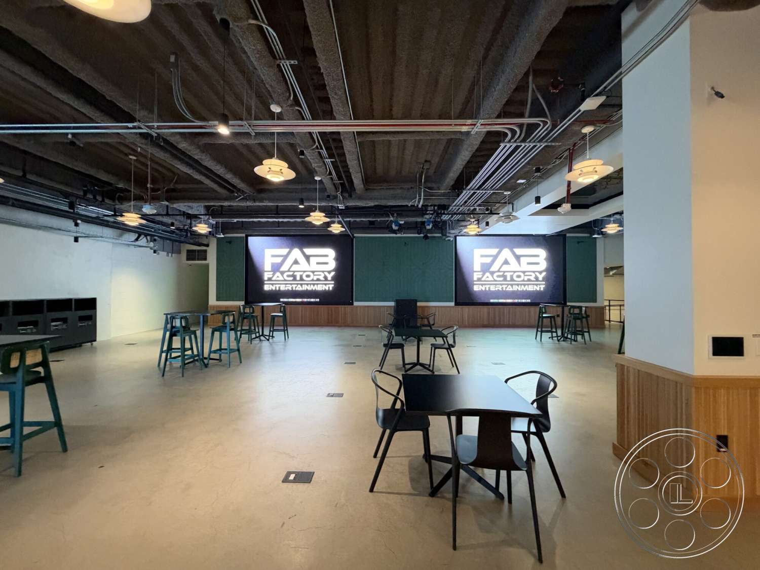 Office 130 - neutral color palette, open floor plan, polished concrete flooring, industrial lighting fixtures, metal bar stools, large projection screen, black metal dining chairs, rectangular seating arrangement, wood panel accent wall, exposed ductwork ceiling, modern design aesthetic